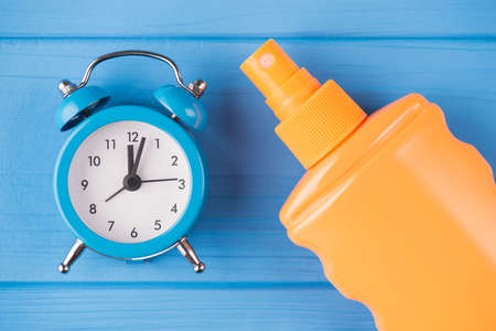 Sunbathing with care concept. Top above overhead view close-up photo of sunscreen and clock isolated on blue wooden backgroundの写真素材