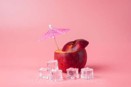 Close-up photo of cut apple with a cocktail umbrella in it and melting ice cubes isolated on pink background with copyspaceの写真素材
