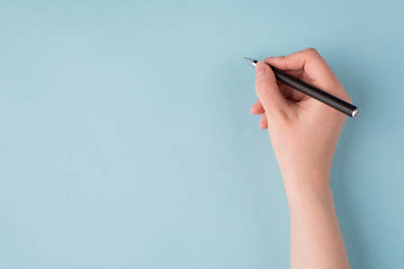 Top above overhead close up first person view photo of girl's right hand holding black pen starting to write isolated over blue color pastel backgroundの写真素材