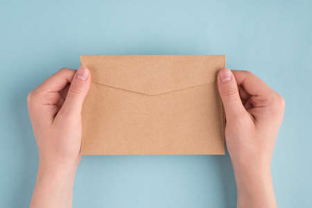 First person people above top overhead close up view photo of female woman hands holding one envelope in hands isolated over pastel color blue backgroundの写真素材
