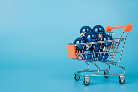 Full length size photo of small metal silver trolley cart full of little toy dark blue baubles isolated of pastel color blue backgroundの写真素材