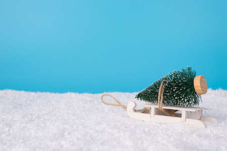 Happy 2021 new year concept. Photo of toy little christmas tree and small sledges on soft shiny snow and light cloudless sky empty blank space for textの写真素材