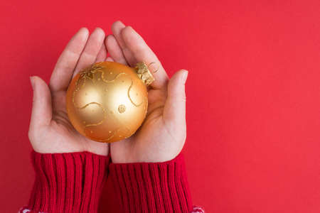 Top above overhead view photo of female hands in sweater holding golden bauble isolated on red background with copyspaceの写真素材