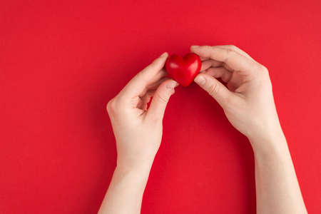 Love and romance concept. Top above overhead view photo of female hands holding red heart isolated on red background with copyspaceの写真素材