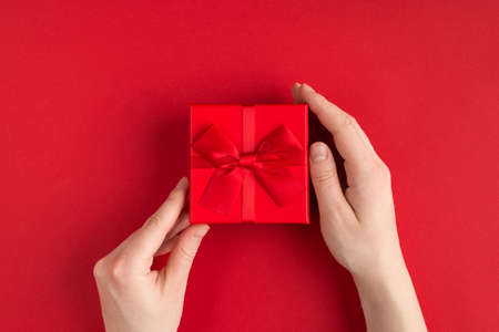 Valentine's day concept. Top above overhead view photo of female hands holding red giftbox with red...