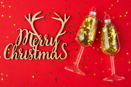 Christmas concept. Top above overhead view photo of wine glasses with golden confetti inside and wooden handmade merry christmas sign isolated on red backgroundの写真素材