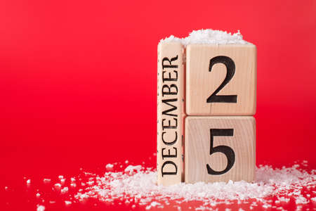 Close up photo of wooden cube calendar showing date of christmas isolated on red background with snowの写真素材