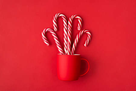 Fountain in cup or dropped christmas mug message concept. Photo of stylish fun bright tea cup with falling hard striped candy canes isolated vivid backgroundの写真素材