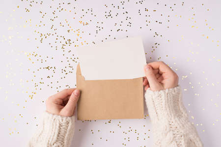 Top above close up overhead view photo of female hands holding kraft paper envelope with mock up copy space card inside over shiny golden background tableの写真素材