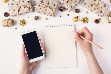 Making wish shopping sale list concept. Photo of female hands holding digital smart phone with touch screen and writing on diary note padの写真素材