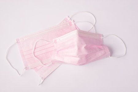 Coronavirus protection concept. Top above overhead close up view photo of pastel pink face mask isolated white background tableの写真素材