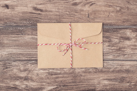 Top above close up photo image of old craft envelope tied up with striped string on wood timber...