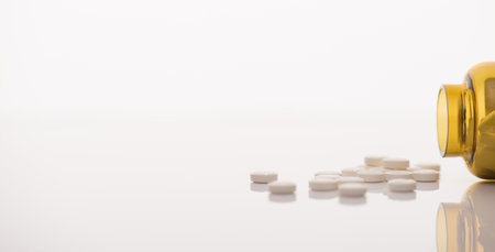 Side profile close up horizontal panoramic banner view photo of yellow glass jar ans pile stack heap of white round pills isolated backdrop with space for textの写真素材