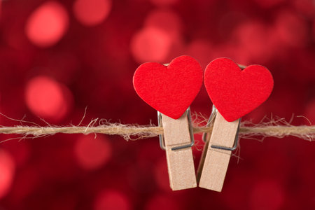Happy Saint valentines day concept. Close up view photo of two lovely clothespins hanging on rope with bokeh red shiny backdropの写真素材