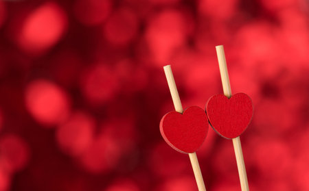 Happy Saint valentines day concept. Close up photo of two wooden heart shaped sticks on red shimmer bokeh backdropの写真素材
