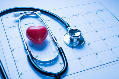 Visit to cardiologist concept. Close up view photo of doctor's stethoscope with red small hear lying on calendar workplaceの写真素材