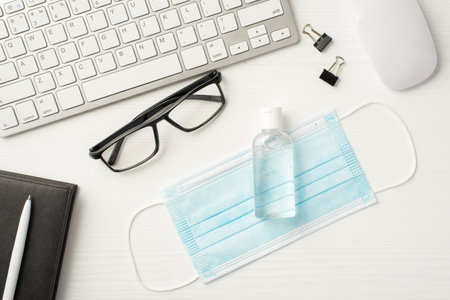 Stay safe at work concept. Top above overhead flat lay photo of office workplace with surgical filter mask and antiseptic laying on wooden white deskの写真素材