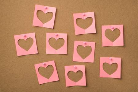 St valentines day concept. Photo of pastel pink notepaper with cut hearts attached to the wooden...