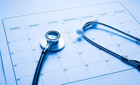 Appointment with a doctor concept. Close up photo of paper blank calendar with medical tool stethoscope on practitioner's tabletopの写真素材