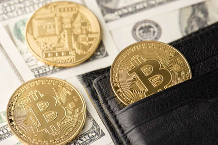 Close up photo of golden glowing shiny bitcoin laying in black open wallet purse and on stack pile...