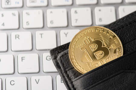 Earning bitcoin concept. Top overhead close up view photo image of golden shiny bitcoin laying in pocket of wallet with white keyboard buttons on the backgroundの写真素材