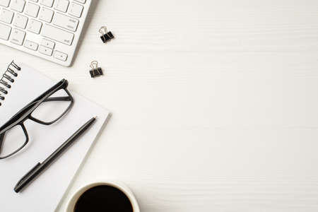 Close up flatlay view photo of white keyboard paperclips open spiral clear copybook eyewear and cup...