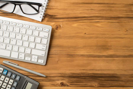 Above overhead close up view photo of pc keyboard eyeglasses calculator and notebook isolated loft wooden brown backdrop with empty spaceの写真素材