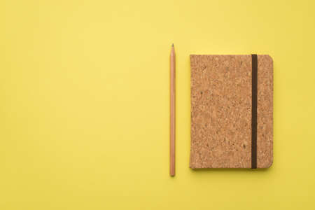 Photo overhead of wood notebook and pencil isolated on the yellow background