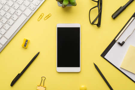 Photo above of phone keyboard glasses paperclips pen notes plant sharpener and glasses isolated bright color yellow backdropの写真素材
