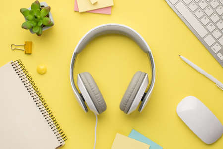 Photo above of headphones plant keyboard notebook pen notes paperclips and computer mouse isolated on the yellow backgroundの写真素材