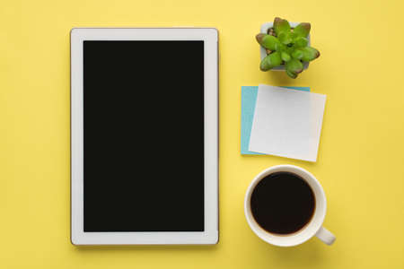 Photo overhead of cup of coffee plant notes and tablet isolated on the yellow background