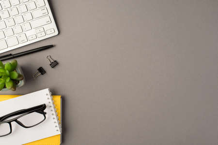 Above photo of notebook black pen paperclips keyboard plant and glasses isolated on the gray...