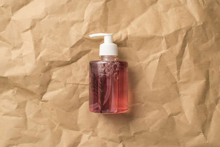 Top view photo of natural pink liquid care product in transparent bottle with copyspace on isolated crumpled craft paper backgroundの写真素材