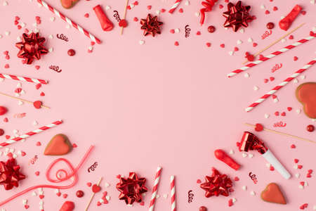 Top view photo of birthday composition with red ribbon stars serpentine confetti heart-shaped cookies bright decorations with copyspace in the middle on pastel pink backgroundの写真素材