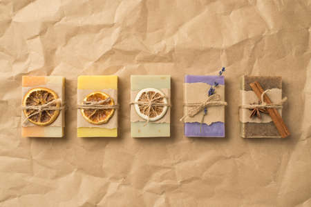 Top view photo of organic solid care products lying in row in paper wrapping and twine with dried citrus slices lavender cinnamon on isolated crumpled craft paper background with copyspaceの写真素材