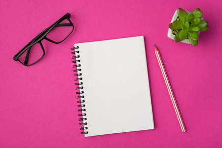 Top view photo of workplace with glasses plant pencil and notebook on isolated pink background with copyspaceの写真素材
