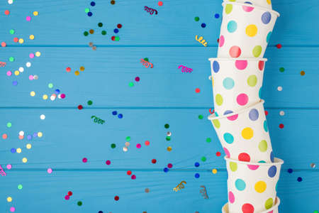 Top view photo of birthday party composition confetti and polka dots paper cups on the right on isolated blue wooden table background with copyspace on the leftの写真素材
