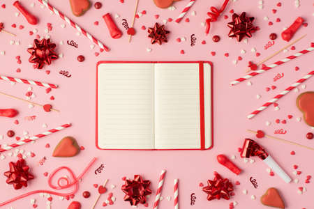 Top view photo of birthday composition with red ribbon stars serpentine confetti bright decorations and red open planner in the middle with copyspace on pastel pink backgroundの写真素材