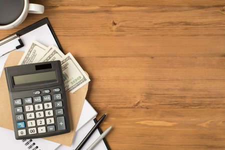 Above photo of calculator notebook clipboard two pens envelope with money dollars and cup of coffee isolated on wooden backdropの写真素材