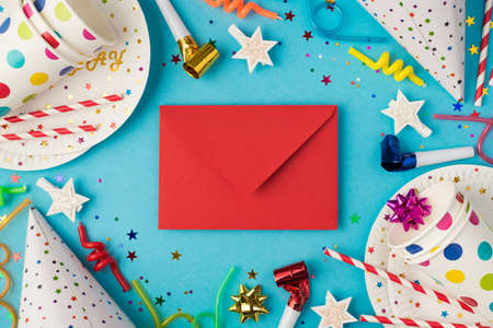 Top view photo of birthday party table composition closed red envelope in the middle candles pipes spiral straws hats sequins polka dots paper cups and plates on isolated blue backgroundの写真素材
