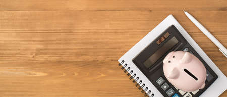 Top view photo of workplace with pen piggy bank and calculator on notebook on isolated wooden table background with copyspaceの写真素材