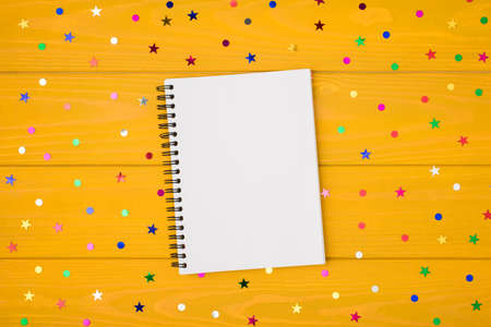 Above photo of empty blank mockup notebook with multicolored confetti isolated on the yellow wooden backgroundの写真素材