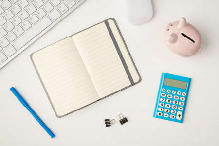 Top view photo of business workplace with keyboard mouse piggy bank binders open gray planner with copyspace blue calculator and pen on isolated white backgroundの写真素材