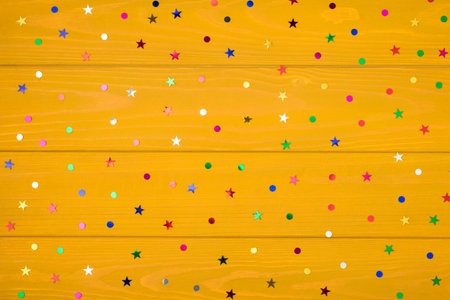 Above photo of multicolored rainbow confetti isolated on the yellow wooden background with empty...