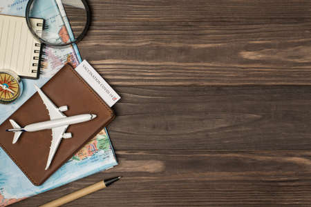 Top view photo of map magnifier compass notebook pen and airplane model on leather passport cover with vaccination certificate on isolated wooden table background with copyspaceの写真素材