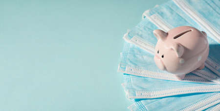 Overhead photo of piggybank pink pig with pile of masks isolated on the blue backgroundの写真素材