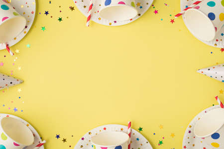 Above photo of cups drink cocktail soda multicolored glitter confetti birthday hat and plates isolated on the yellow background with copyspaceの写真素材