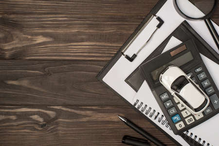 Top view photo of workplace with chancellery black folder organizers magnifier calculator pen and car model on isolated wooden table background with copyspaceの写真素材