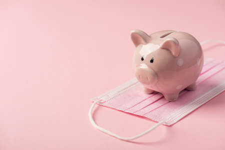 Closeup photo of piggy bank on medical mask isolated pink background with copyspaceの写真素材