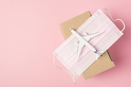 Overhead photo of airplane and box humanitarian aid donation with face mask isolated on the pink...